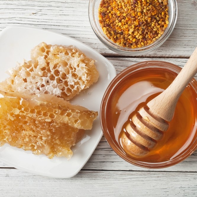 Honig, Honigwabe, Bienenpollen, Honiglöffel auf Holzuntergrund