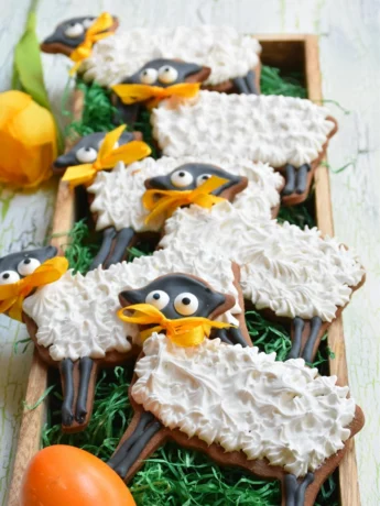 Osterlämmchen aus Mürbteig mit royal Icing auf grünem Hintergrund in Holzschale