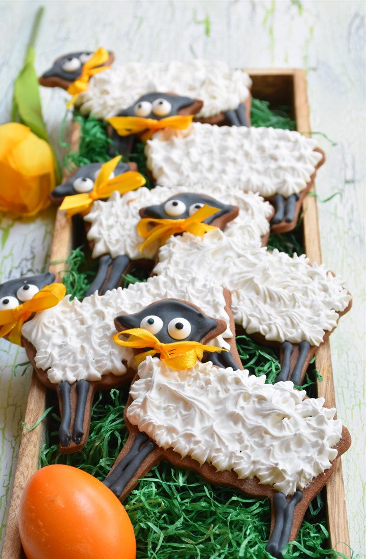 Osterlämmchen aus Mürbteig mit royal Icing auf grünem Hintergrund in Holzschale